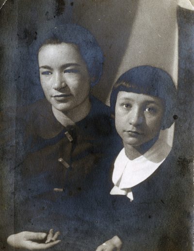 Nina Kosterina at 18 with dark hair wearing a dark jacket, sitting next to her younger sister Elena with short dark hair and a dark dress with a white collar.