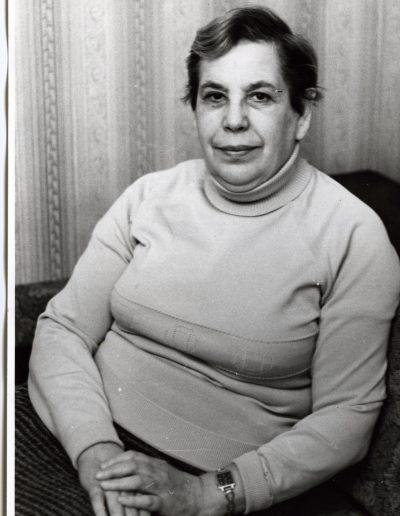 Older woman with short gray hair posing for a picture, smiling, wearing a light-colored turtleneck sweater