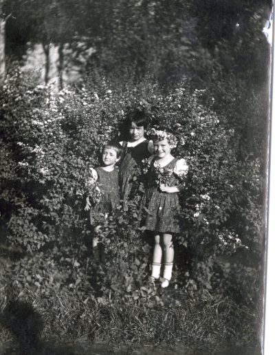 Three girls posing in a country setting in dresses and carrying or wearing flowers