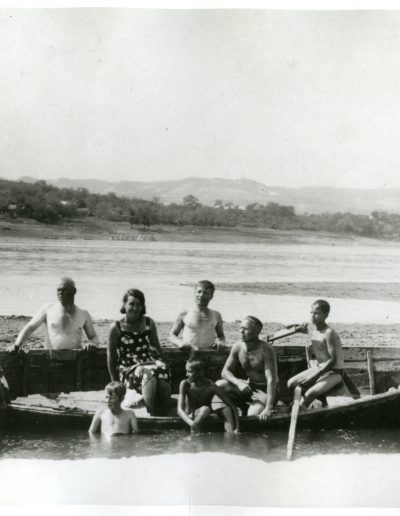 Several family members sitting in a large canoe. Nina is wearing a white sun dress and white cap.